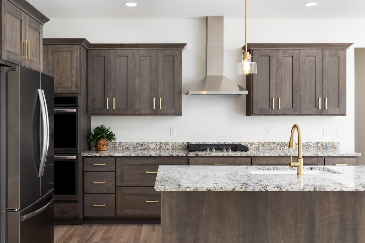 A premium custom kitchen with dark timber cabinetry, stone benchtops and brass detailing